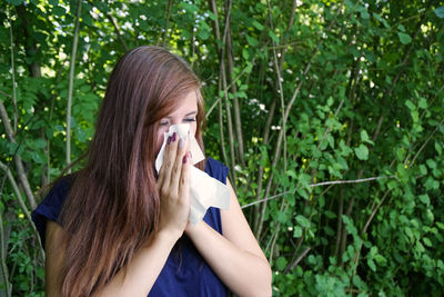 Young woman by plants blowing nose