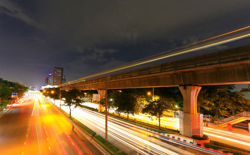 Light trails on road by bridge against sky in city at night
