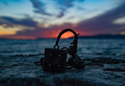 Close-up of metal chain on beach against sky during sunset