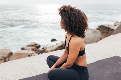 Rear view of woman sitting on rock at beach