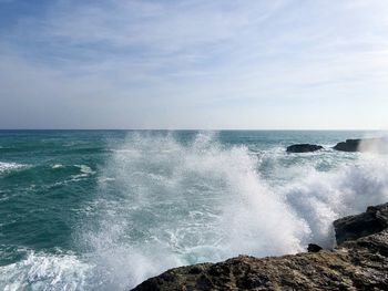 Waves splashing on rocks against sky