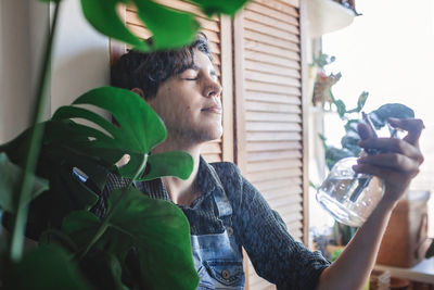 Young girl spraying water for home plants on herself, green environment in room, home gardening