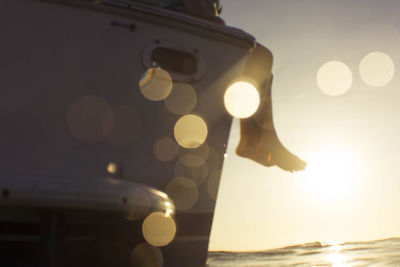 Low section of woman sitting on boat in sea during sunset