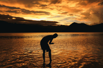 Silhouette man standing on beach against sky during sunset