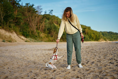 Full length of eoman standing on beach, waking with dog