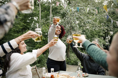Cheerful friends celebrating while toasting drinks with each other during dinner party