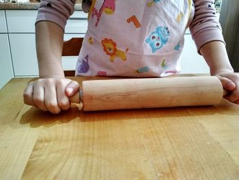 Midsection of woman holding rolling pin at table in kitchen