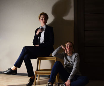 Portrait of young couple sitting on chair against wall