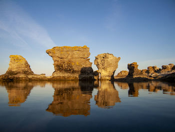Reflection of rauk rock formations in water against clear blue sky