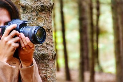 Man photographing through tree trunk in forest
