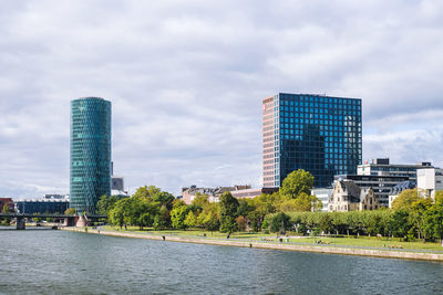 Modern buildings by river against sky in city