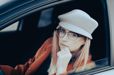A stylish middle-aged woman wearing a gray hat and glasses sits behind the wheel of her car