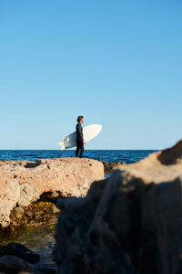 Man on rock at beach against sky