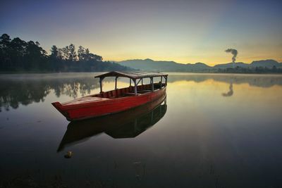 Boat moored on lake against sky during sunset