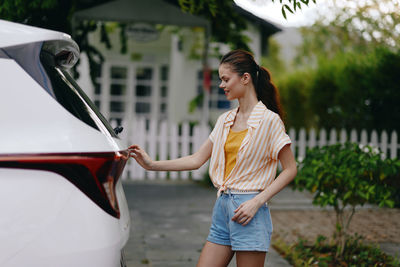 Side view of young woman standing in car