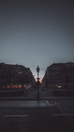 Road by buildings against sky in city at dusk