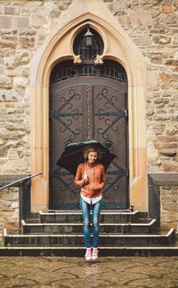 Smiling woman with umbrella in mid-air against entrance of old building