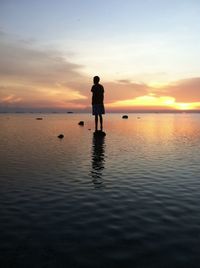 Silhouette man standing in sea against sky during sunset