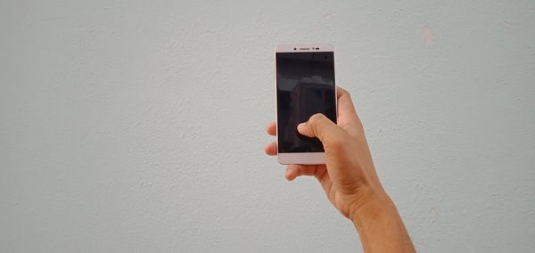Midsection of person holding mobile phone against wall