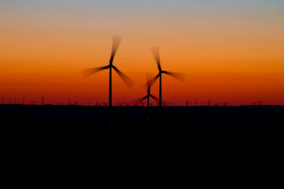 Silhouette wind turbines on field against orange sky