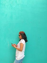 Woman using phone while standing against wall