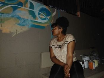 Young woman looking down while standing against wall