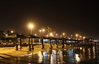 Illuminated pier over sea against sky at night