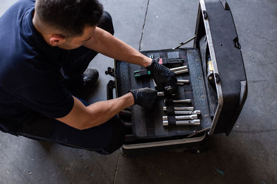 From above male technician picking screwdriver bits from tool box while working in garage