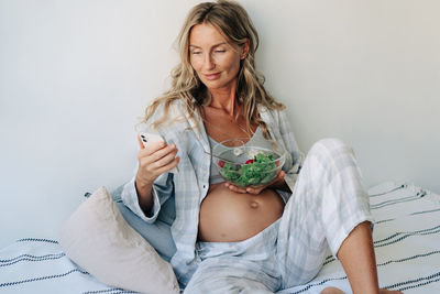 A pregnant woman eats salad and chats online on the internet.