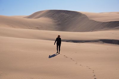 Rear view of woman walking on sand dune in desert