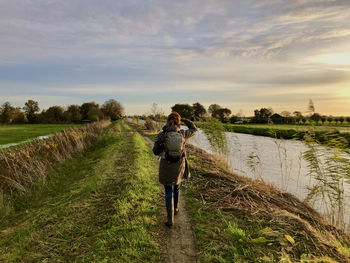 Rear view of a woman walking along a canal in the farmland at sunrise