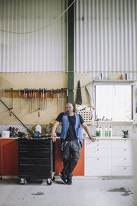 Full length of mature carpenter standing by workbench at workshop