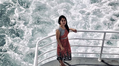 Portrait of a young woman standing against railing