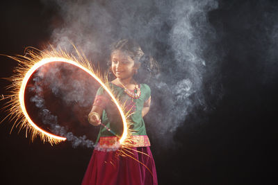 Girl spinning sparkler while standing against black background