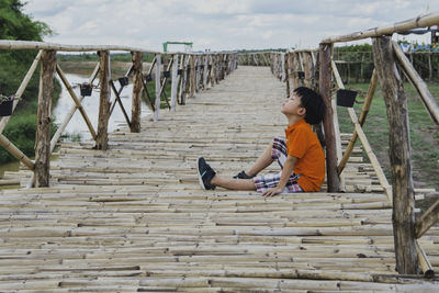 Side view of boy sitting on wooden footbridge