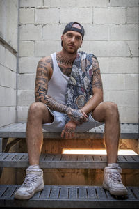 Full length portrait of young man sitting against wall