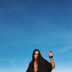 Low angle portrait of young woman against blue sky