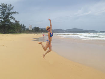 Young woman jumpimg on the beach on a cloudy day, phuket, thailand