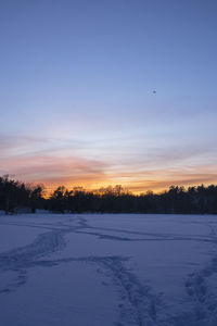 Snow covered landscape against sky during sunset