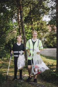 Full length portrait of smiling boys walking with garbage bags