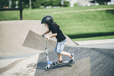 Side view of boy riding push scooter on sports ramp in park