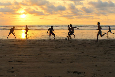 Silhouette children playing on beach against sky during sunset