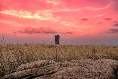 Lighthouse on field against sky during sunset