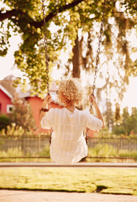 Rear view of girl with curly blond hair playing on swing at yard