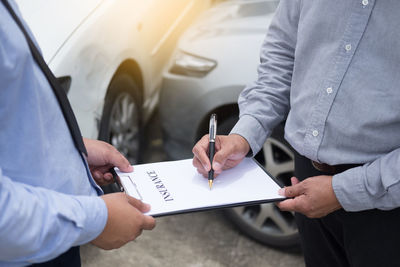 Midsection of customer signing on insurance paper with man