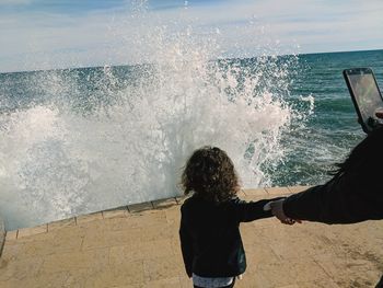 Rear view of people by sea against sky