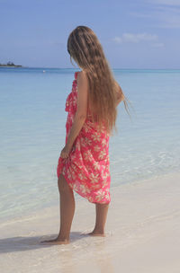 Rear view of girl wearing beachwear standing at shore against sky