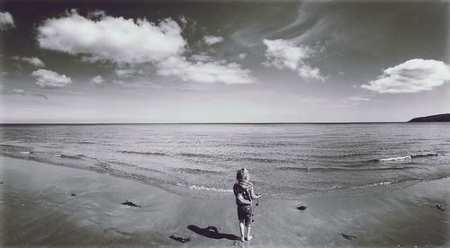 Child standing at beach against sky on sunny day