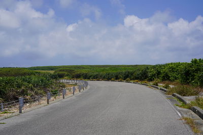 Empty road along plants and trees against sky