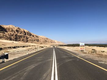 Road leading towards mountains against clear blue sky